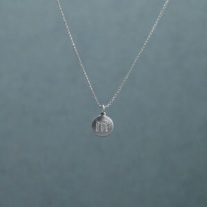 Silver necklace with a circular pendant embossed with the letter “m” 