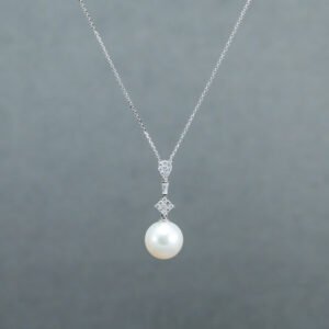 A white pearl is hanging from the side of a silver chain.
