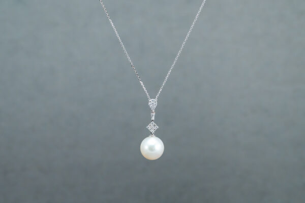 A white pearl is hanging from the side of a silver chain.