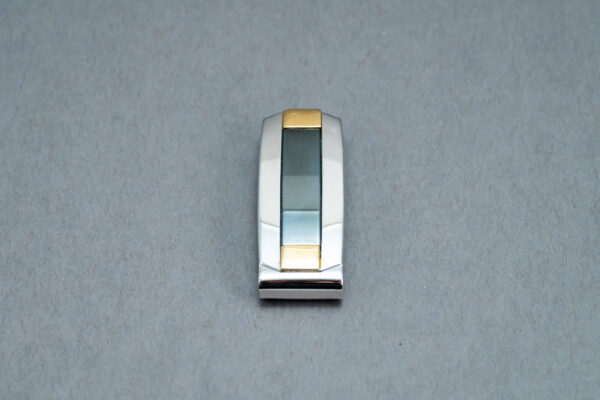 A silver and gold clip on the side of a white wall.