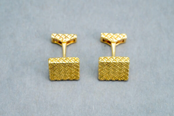 A pair of gold cufflinks with a square design.