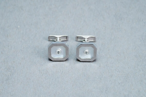 A pair of silver cufflinks with a diamond on each side.