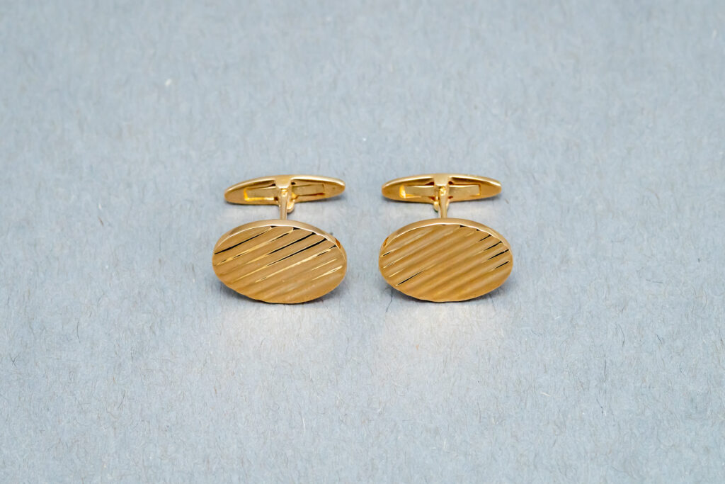 A pair of gold cufflinks with diagonal lines.