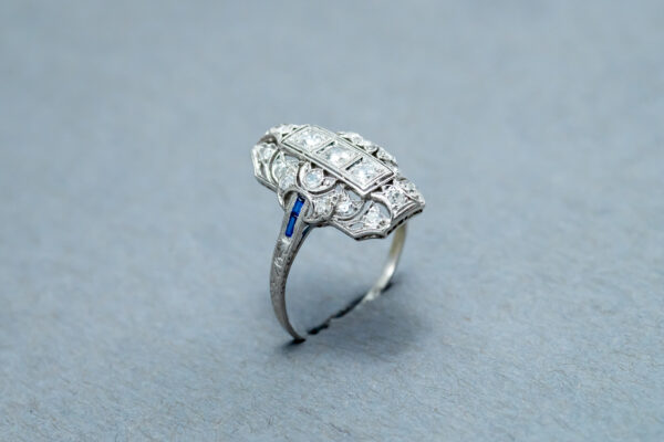 A diamond and sapphire ring is shown on top of a gray surface.