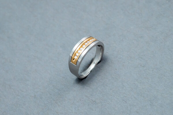A silver ring with gold inlay on top of a gray surface.