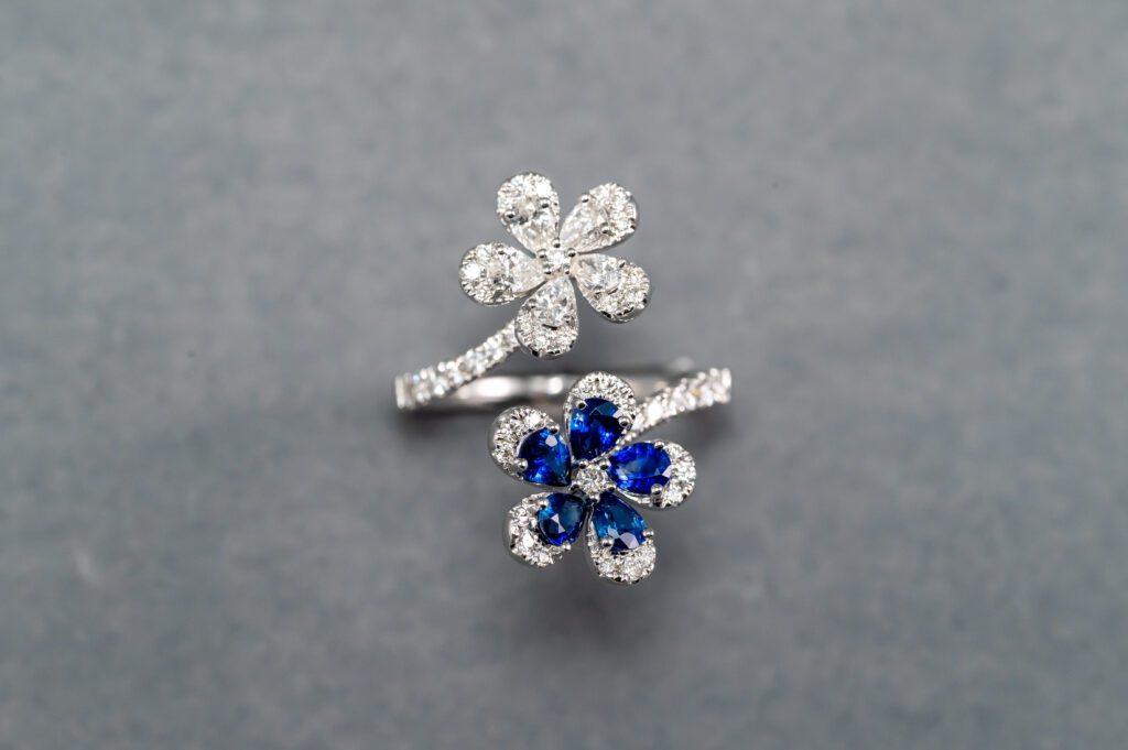 A silver ring with two flowers and blue stones.