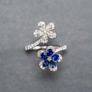 A silver ring with two flowers and blue stones.