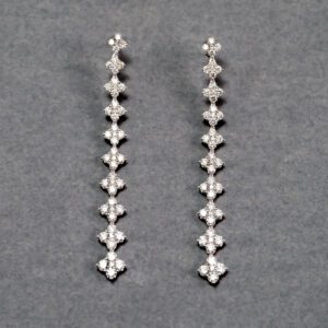 A pair of long diamond earrings on a gray surface.