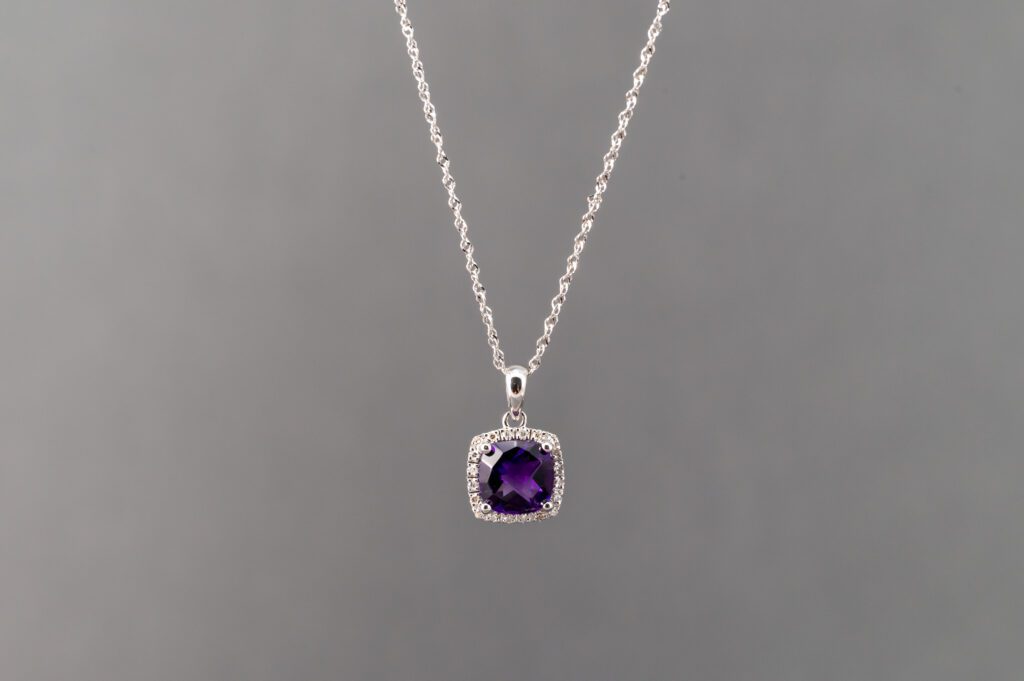 A silver necklace with a purple stone on it.
