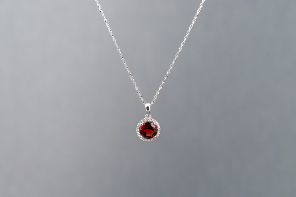A silver necklace with a red stone on it.