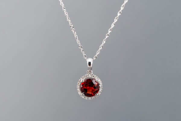 A silver necklace with a red stone on it.