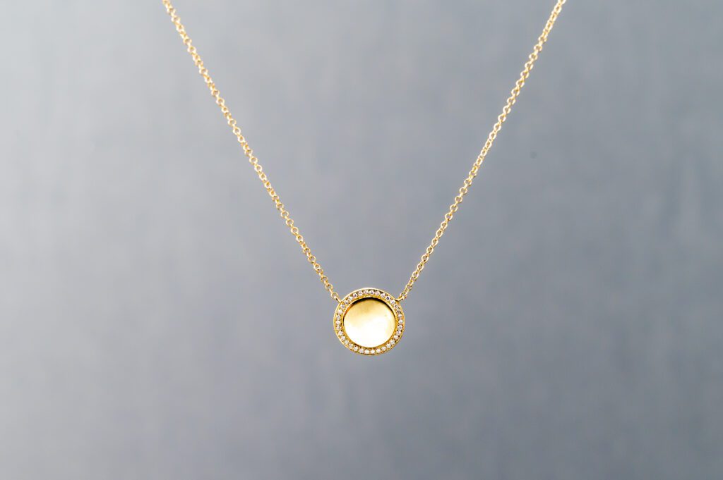 A gold necklace with a round pendant on it.