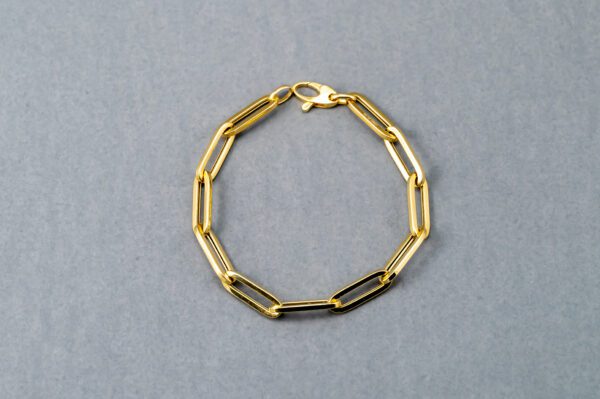 A gold chain link bracelet is shown on top of a gray background.