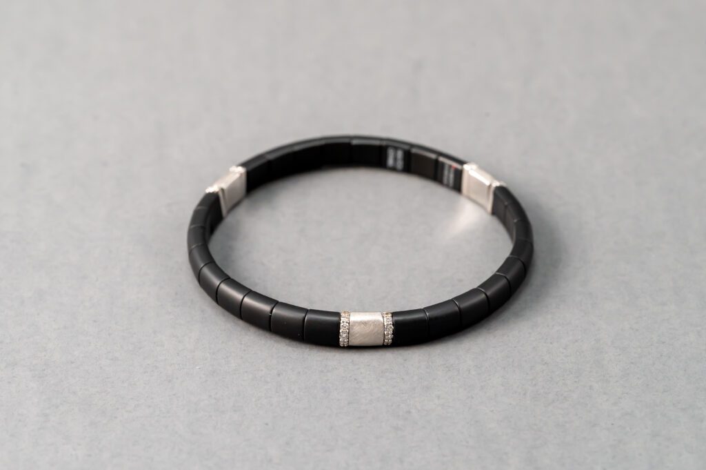 A black bracelet with silver accents on top of a gray surface.