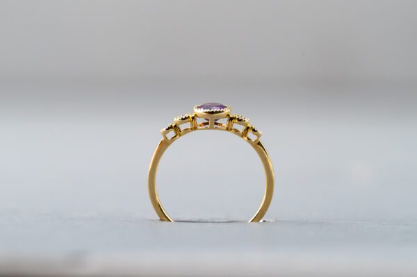 A gold ring with a purple stone on it's side.