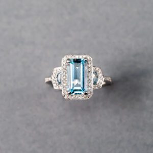 A blue topaz and diamond ring is shown on top of a gray background.