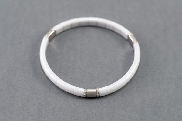 A white bracelet with silver accents on it.