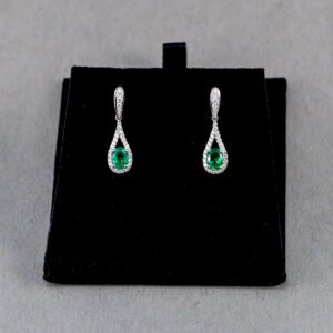 A pair of earrings with green stones on top of black velvet.