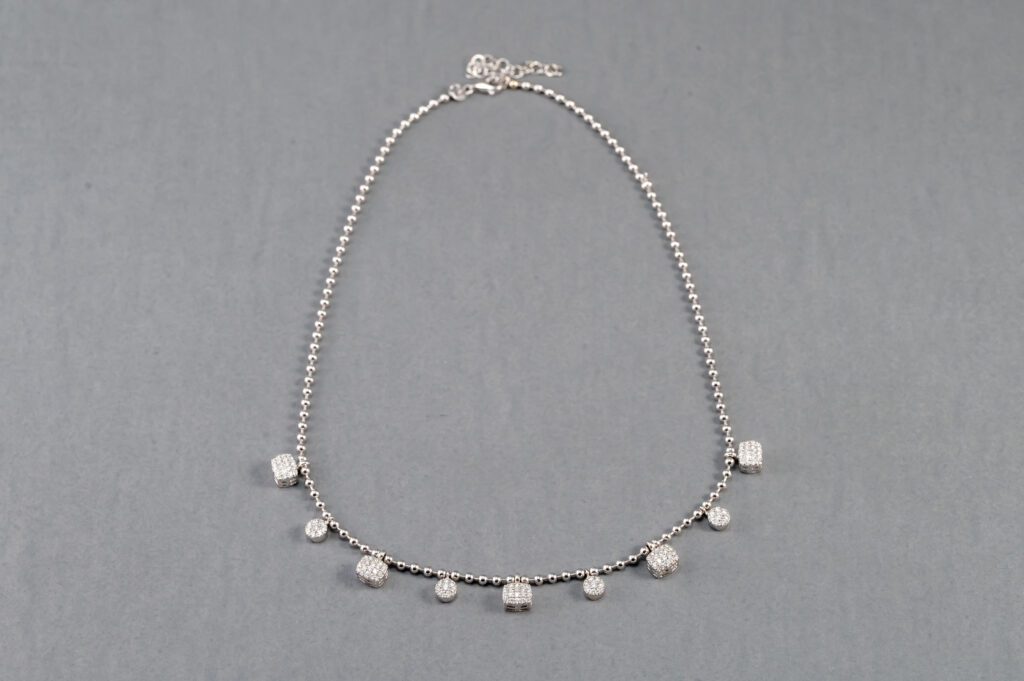 A silver necklace with small white beads on it.
