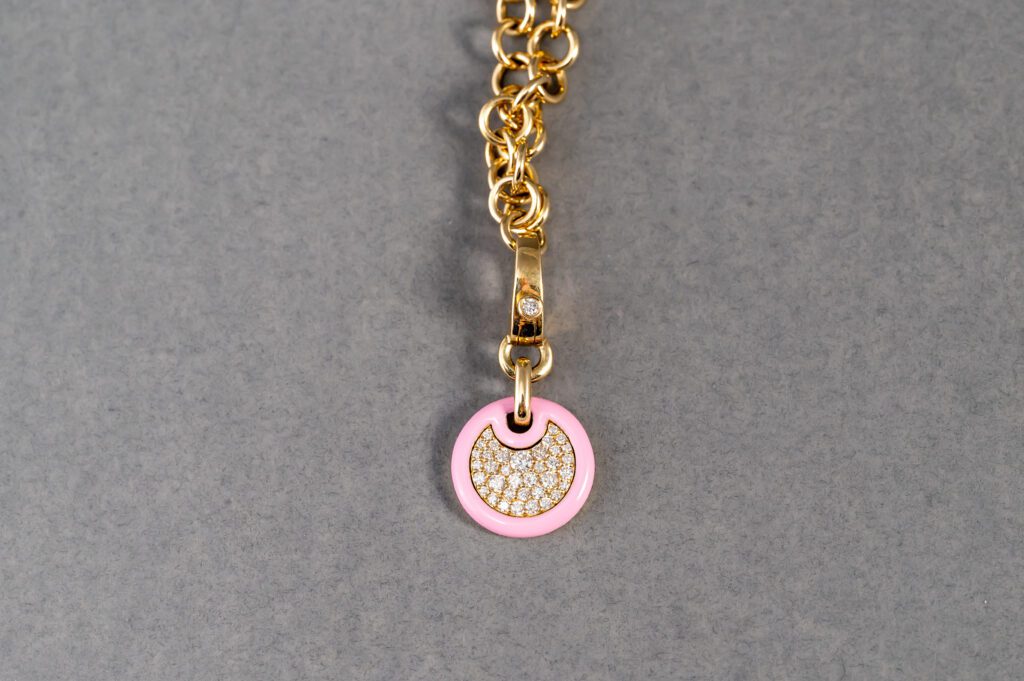 A gold chain with a pink and white pendant on it.